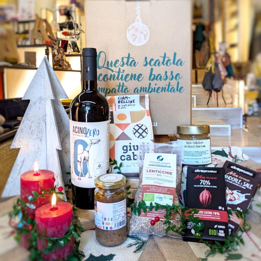 Immagine dei prodotti nel cesto Terre dell'Umbria solidale, prodotti umbri e del commercio equo e solidale. In primo piano biscotti, vino rosso umbro, cioccolato mascao, miele millefiori umbro, cioccolata in tazza fondente bio Altromercato.
